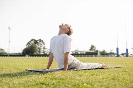 surface level of young yoga man practicing cobra pose with closed eyes on green grass outdoorsの写真素材