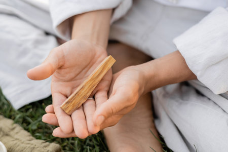 partial view of man in white linen clothes holding aromatic palo santo stick while sitting outdoorsの写真素材