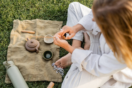 top view of yoga man holding scented stick near linen rug with clay teapot and bowls on grassy lawnの写真素材