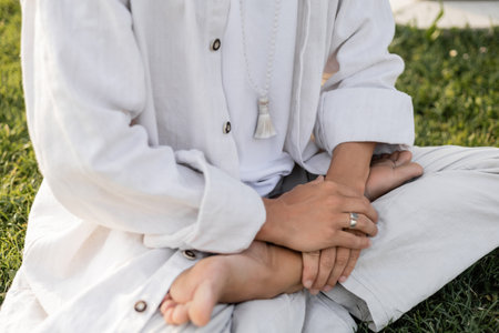 cropped view of man in white clothes sitting in lotus pose during meditation outdoorsの写真素材
