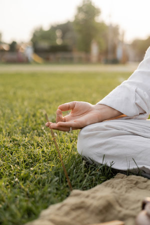 cropped view of man in white linen clothes meditating with gyan mudra gesture while sitting on green grassy fieldの写真素材