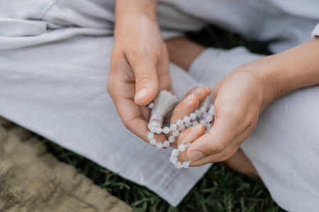 cropped view of young man holding mala beads while meditating outdoorsの写真素材
