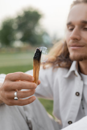 smoldering aromatic stick in hand of blurred man meditating outdoorsの写真素材