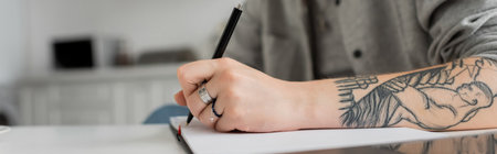 cropped shot of young woman with tattoo on hand writing in notebook, taking notes, having...