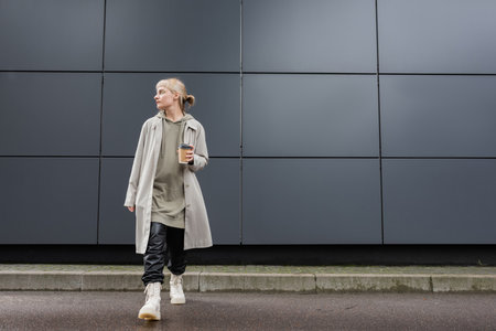 full length of young woman with blonde hair with bangs walking in coat, black leather pants, hoodie...