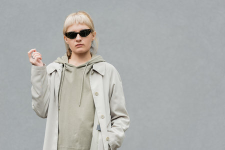 stylish and young woman with bangs and blonde hair standing in trendy sunglasses and comfortable...