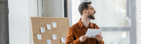 accomplished and happy bearded businessman in eyeglasses and stylish shirt looking away near...