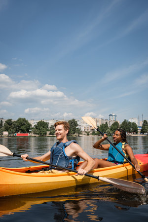 positive and active multiethnic couple in life vests spending recreation weekend by sailing in...