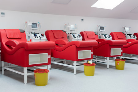 row of modern and comfortable medical chairs near transfusion machines with touchscreens, drip stands with infusion bags, trash buckets in sterile environment of blood donation centerの写真素材