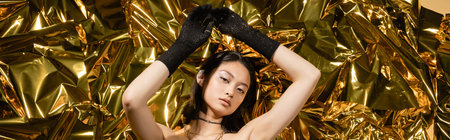 asian young woman with wet hairstyle and short hair posing in black gloves while standing with...