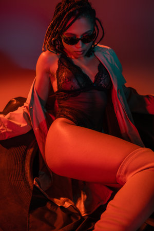 sassy and sexy african american woman in dark stylish sunglasses, black lace bodysuit and beige...