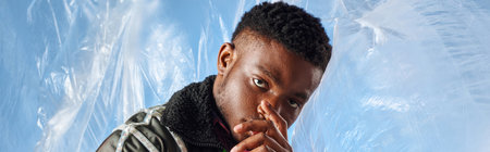 Good looking afroamerican model with trendy hairstyle covering face and wearing outwear jacket with...