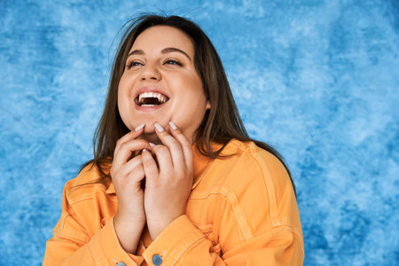 portrait of body positive and happy plus size woman with brunette hair and natural makeup laughing...