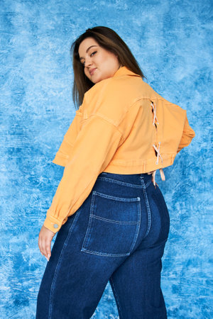 alluring plus size woman with long hair and natural makeup wearing crop top, orange jacket and denim...