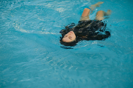 summer getaway, carefree woman in black swimwear swimming in blue water of public swimming pool in...