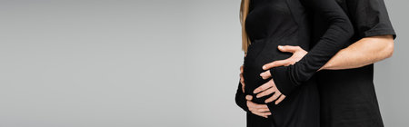 Cropped view of man in t-shirt hugging and touching belly of stylish pregnant wife in black dress...