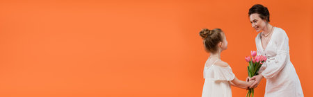 Mother`s day, preteen girl giving bouquet of flowers to smiling mother on orange background, bonding, white dresses, pink tulips, happy holiday, vibrant colors, joyful occasion, bannerの写真素材