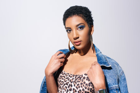 Young and short haired african american woman with blue eyeshadow and golden earrings posing in top...