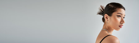 profile portrait of young asian woman with brunette hair, bold makeup, trendy hairstyle posing in silver necklaces and looking away on grey background, stylish spring, fashion photography, bannerの写真素材