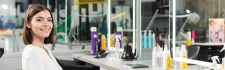 customer in salon, tattooed young woman sitting in chair and looking at camera near hair salon tools, beauty service, hair extension, hair coloring,  blurred background, generation z, bannerの写真素材