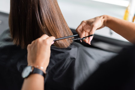hairdo, cropped view of hairdresser cutting short brunette hair of female client, holding scissors and comb, professional, beauty worker, haircut, salon job, salon customerの写真素材