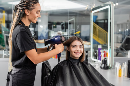 salon blow dry, professional beauty worker with round brush and hair dryer styling hair of female customer, brunette woman with short hair, beauty salon, client satisfaction, hair volume, blowoutの写真素材