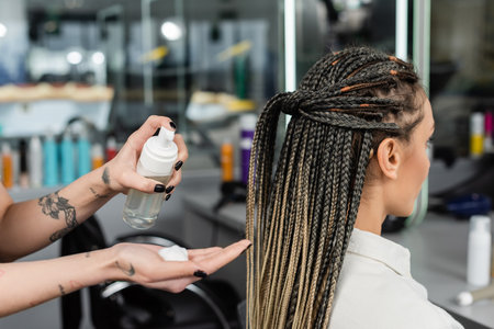 client satisfaction, hair product, tattooed hairdresser with styling foam in hand, woman with braids in salon, bottle, beauty worker, salon customer, beauty worker, hair professionalの写真素材