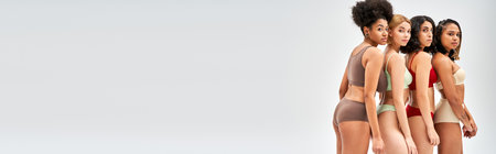 Multiethnic women in colorful and stylish lingerie standing next to each other and looking at camera isolated on grey, different body types and self-acceptance concept, multicultural models, bannerの写真素材