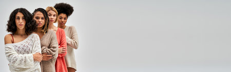 Confident multiethnic women in knitted jumpers crossing arms and posing isolated on grey, different body types and self-acceptance, multicultural representation, banner with copy spaceの写真素材