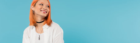 positivity, cheerful asian young woman with dyed hair standing in casual attire and smiling on blue background, white shirt, looking away, choker necklace, red hair, generation z, bannerの写真素材