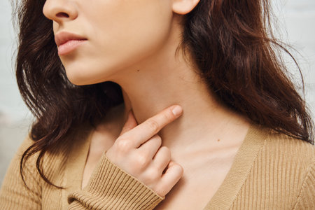 Cropped view of young brunette woman doing self-massage of thyroid gland on neck and lymphatic circulation at home, self-care ritual and holistic wellness practices concept, tension reliefの写真素材