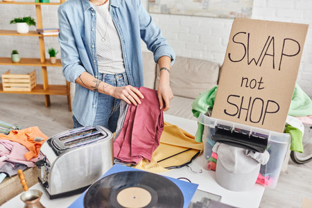 cropped view of tattooed woman with pants near vinyl disc, electric toaster, wardrobe items, plastic box and swap not shop card, exchange market, sustainable living and circular economy conceptの写真素材