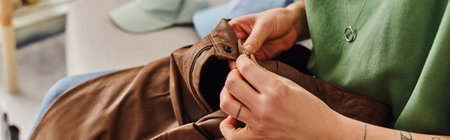 cropped view of young and tattooed woman checking button on leather pants during clothes...