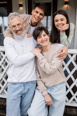 family photo, happy parents day, joyful middle aged parents hugging near daughter and young adult...