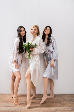 cheerful bride with white flowers, diverse bridesmaids, bridal bouquet, cultural diversity, friendship goals, brunette and blonde women, bridal shower, smile and joy, full lengthの写真素材