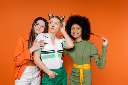 Trendy and multiethnic girlfriends hugging stylish blonde friend pouting lips while posing together...
