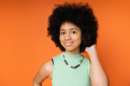 Portrait of smiling and stylish african american teenager with bold makeup wearing necklace and...