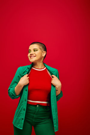 fashion trend, happy and tattooed, short haired woman in green outfit smiling on red background, looking away, generation z, youth culture, vibrant backdrop, individuality, personal styleの写真素材