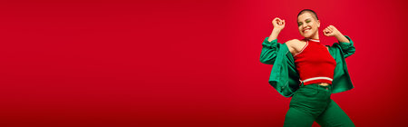 youth culture, stylish appearance, bold makeup, happy and tattooed, short haired woman in green outfit dancing on red background, generation z, youth, modern backdrop, individuality, bannerの写真素材