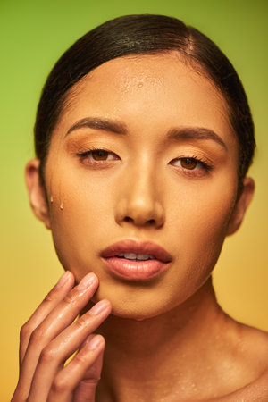 water drops on face, close up of young asian woman with wet skin looking at camera on green background, skin hydration, face care campaign, perfection, wellness, conceptualの写真素材