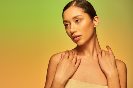 beauty and skin care, pretty asian woman with brunette hair and bare shoulders posing on gradient background, green and orange, skin care, glowing skin, natural beauty, young modelの素材 [FY310207767695]