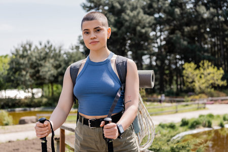Portrait of young short haired and tattooed female tourist with backpack looking at camera while...