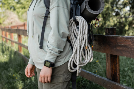 Cropped view of young female hiker with fitness tracker, backpack and travel equipment standing with blurred landscape at background, finding serenity in nature, summerの写真素材