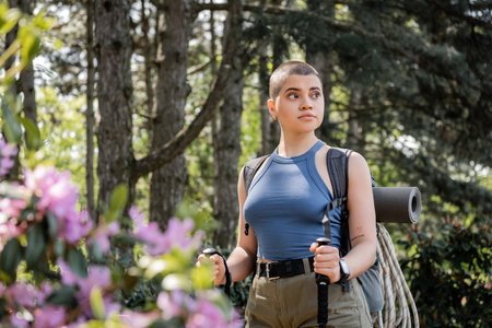Young short haired and tattooed female hiker with backpack and travel equipment holding trekking...