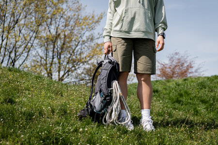Cropped view of young female traveler in casual clothes with fitness tracker holding backpack with...