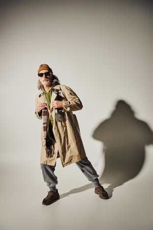 expressive and fashionable personality, full length of senior man in hipster style clothes and dark sunglasses posing on grey background with shadow, positive lifestyle conceptの写真素材