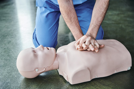 cropped view of professional healthcare worker doing chest compressions on CPR manikin,...