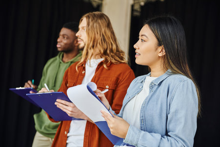 smiling asian woman writing on clipboard near multiethnic and stylish men during first aid seminar in training room, health care and emergency preparedness conceptの写真素材