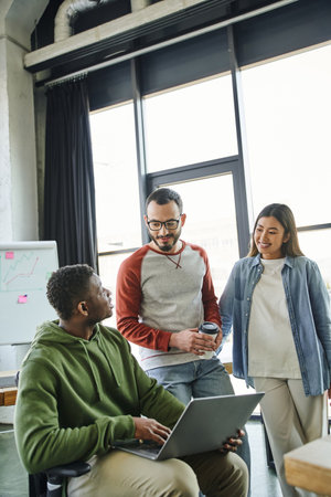 young african american businessman sitting with laptop near positive asian woman and bearded man...