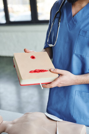 partial view of professional paramedic in blue uniform holding wound care simulator above CPR...